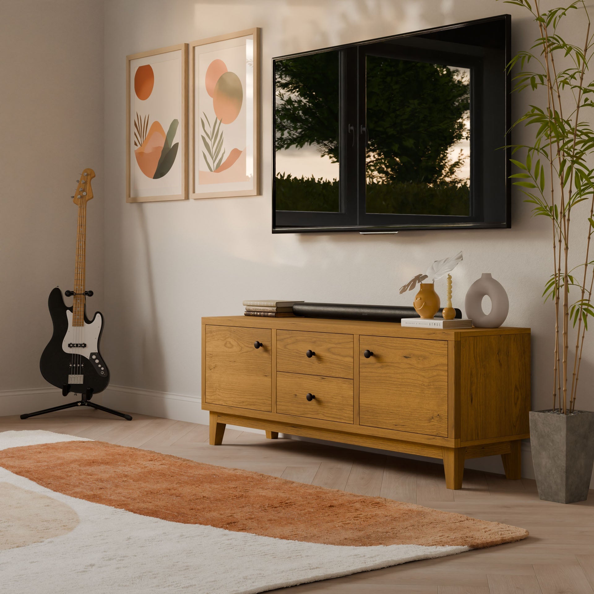 A modern living room showcases a Krovel Furniture Co. Double Drawer, Double Door Media Cabinet in Cherry with soft-close slides. It features a potted plant, a wall-mounted TV, abstract art above, and a guitar in the corner. A brown and white rug accents the light floor while sunlight highlights the hardwood veneer finish.