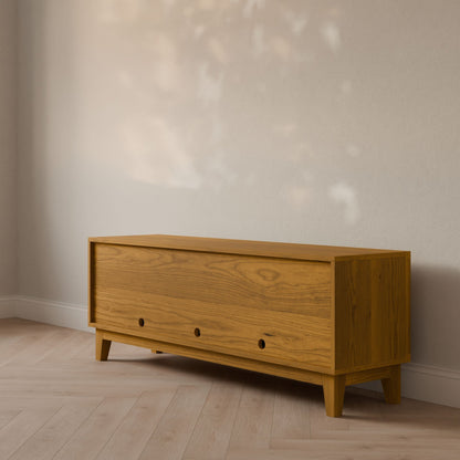 The Maine Made Double Drawer, Double Door Media Cabinet by Krovel Furniture Co. features three round handles and sits against a light wall in a minimalist room with wood flooring and natural light—handmade in Portland, Maine.