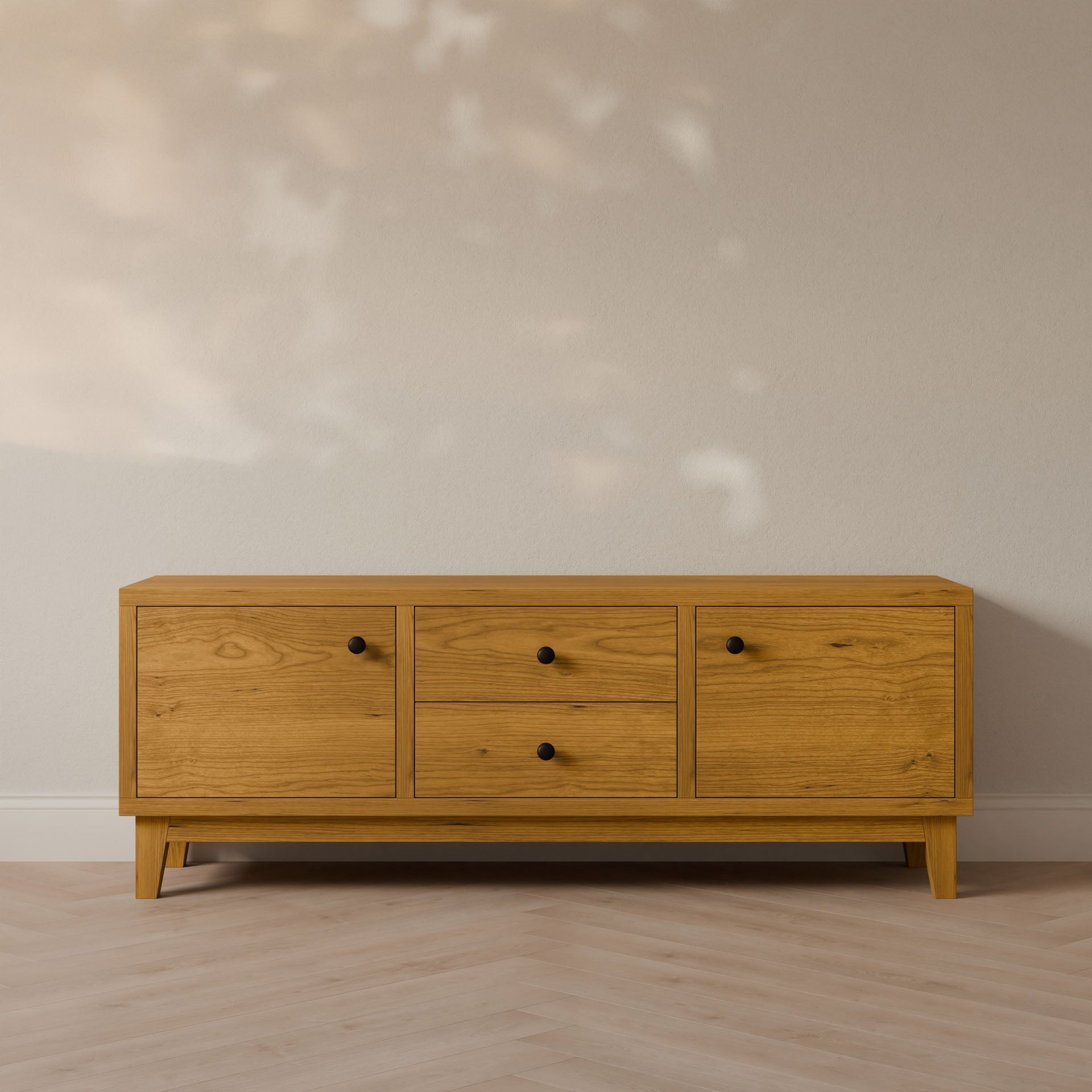 The Krovel Furniture Co. Double Drawer, Double Door Media Cabinet in Cherry stands against a light wall with shadows. It features two side cabinets and central drawers with round black knobs, enhanced by soft-close slides on a light wood herringbone floor.