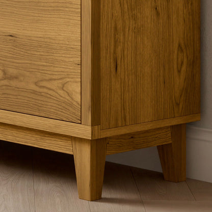 A close-up of the Krovel Furniture Co. Double Drawer, Double Door Media Cabinet in Cherry showcases its short legs and hardwood veneer that highlights a light brown finish with visible grain patterns. The light wood plank flooring enhances the cabinets elegant design.