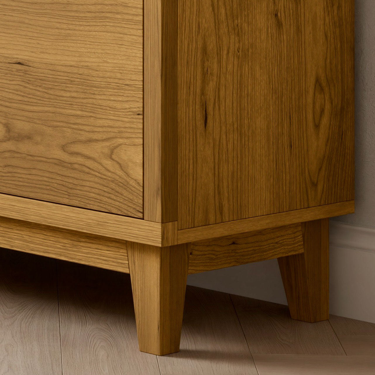 Close-up of the Krovel Furniture Co. Maine Made Double Drawer, Double Door Media Cabinet, featuring a natural grain finish and clean lines, handmade in Portland, Maine, shown on a light wood floor beside a white baseboard.