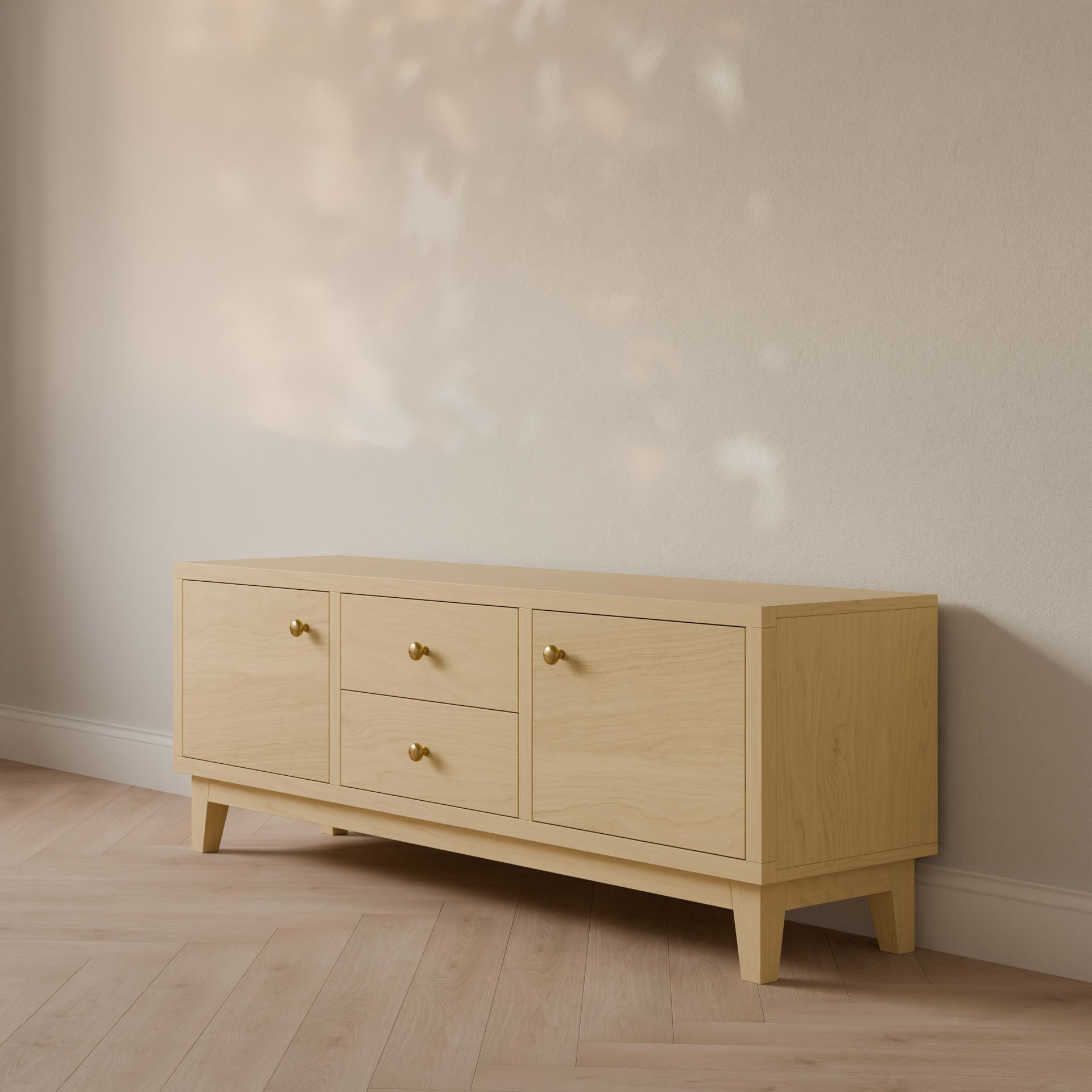The Double Drawer, Double Door Media Cabinet in Maple by Krovel Furniture Co. is a light wooden sideboard handmade in Portland, Maine. It features two cabinets and two central drawers with golden knobs, set against a beige wall. The light wood floor complements this elegant hardwood veneer piece.