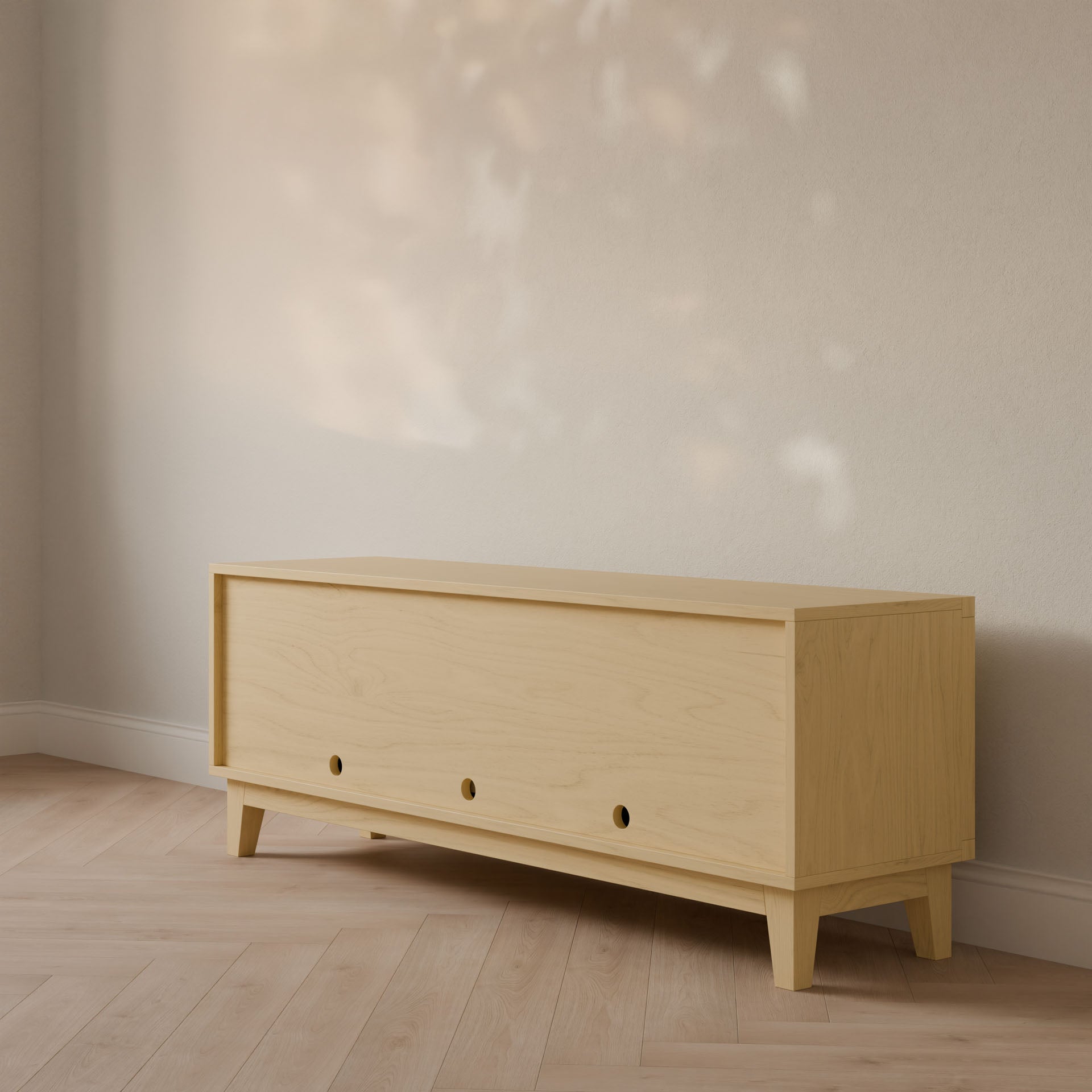 The Double Drawer, Double Door Media Cabinet in Maple by Krovel Furniture Co. sits elegantly against a light-colored wall. With its minimalist design, circular knobs, and hardwood veneer craftsmanship, it creates a warm and inviting atmosphere enhanced by soft lighting.