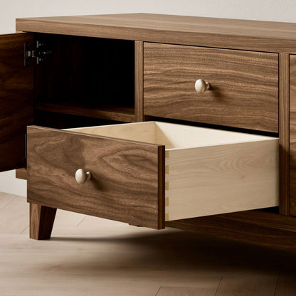 The Double Drawer, Double Door Media Cabinet in Walnut by Krovel Furniture Co. features a handmade hardwood veneer showcasing natural wood grain and round knobs. A solid hard maple drawer is open, and a door is slightly ajar, all resting on a hardwood floor embodying minimalist design.