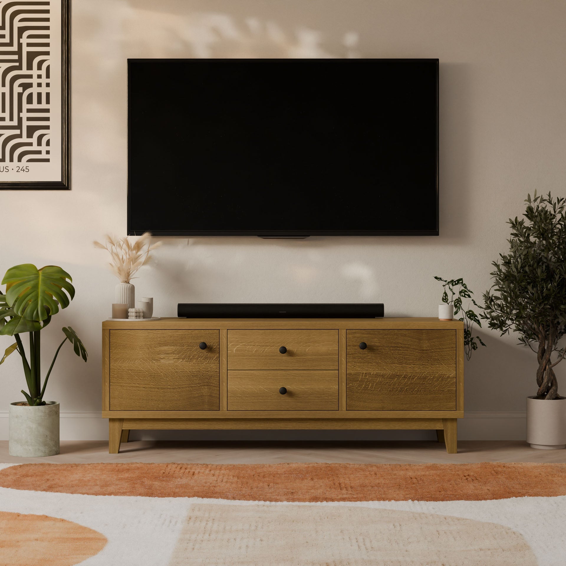 A modern living room features a wall-mounted TV above the Krovel Furniture Co. Maine Made Double Drawer, Double Door Media Cabinet, handmade in Portland, Maine. Potted plants and an abstract rug add charm and style.