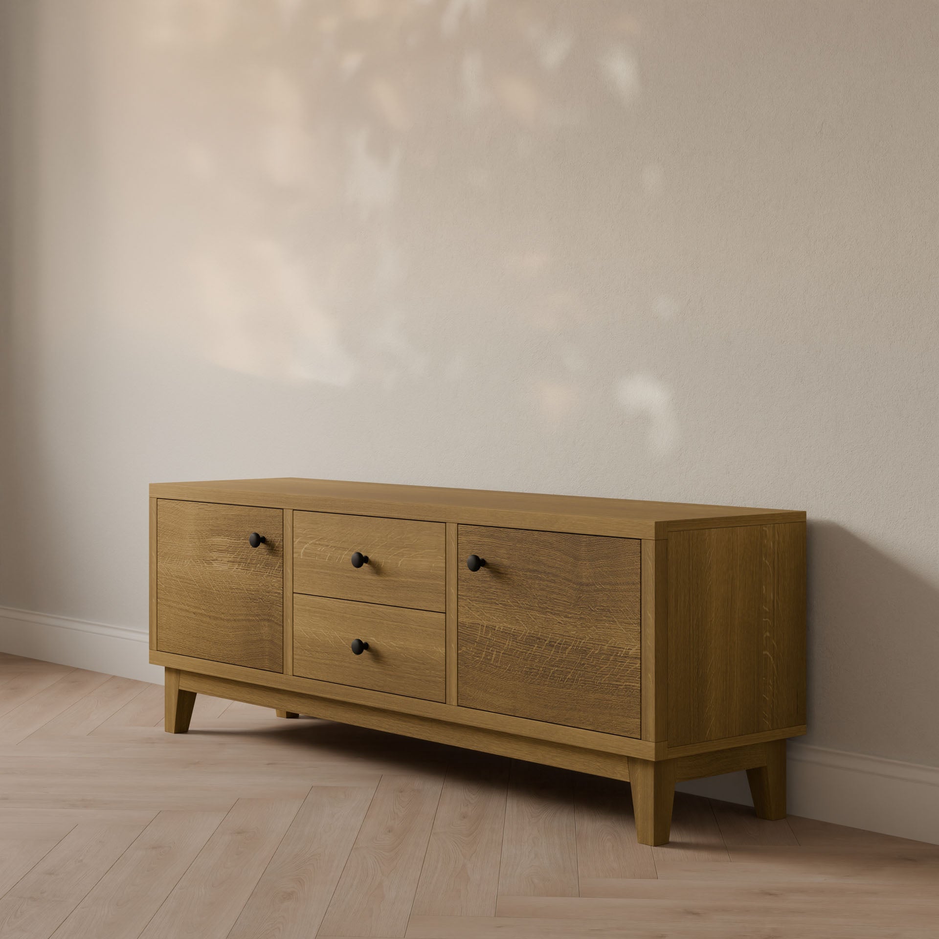 The Double Drawer, Double Door Media Cabinet in White Oak by Krovel Furniture Co. is a minimalist wooden sideboard made from formaldehyde-free hardwood. It includes central drawers flanked by doors and is handmade in Portland, Maine, with soft natural light enhancing its setting against a light wall and wood-patterned floor.
