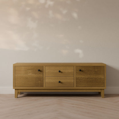 Against a light-colored wall stands the Double Drawer, Double Door Media Cabinet in White Oak by Krovel Furniture Co. Handmade in Portland, Maine, it features formaldehyde-free hardwood construction with two cabinets and central drawers. This minimalist piece is complemented by a herringbone-patterned wood floor.