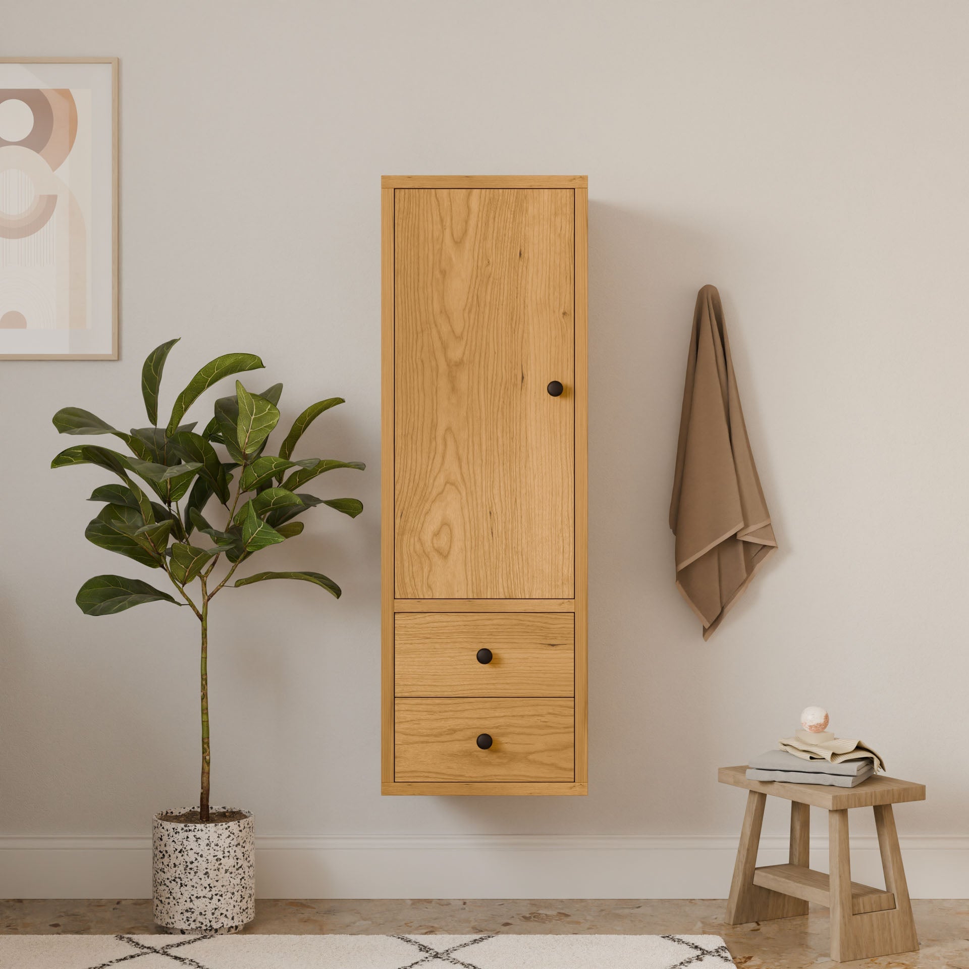 A Krovel Furniture Co. Double Drawer Linen Cabinet in Cherry stands against a beige wall, crafted from sustainable solid hardwood. Nearby, a green plant in a speckled pot breathes life into the area, while minimalist artwork adorns the space. A taupe towel hangs beside a wooden stool with a candle.