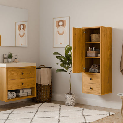 A modern bathroom features a solid hardwood Double Drawer Linen Cabinet in Cherry by Krovel Furniture Co., with neatly stacked towels, a potted plant on the floor, geometric artwork on the walls, a sink with a large mirror, and a basket filled with towels. A patterned rug covers the floor.