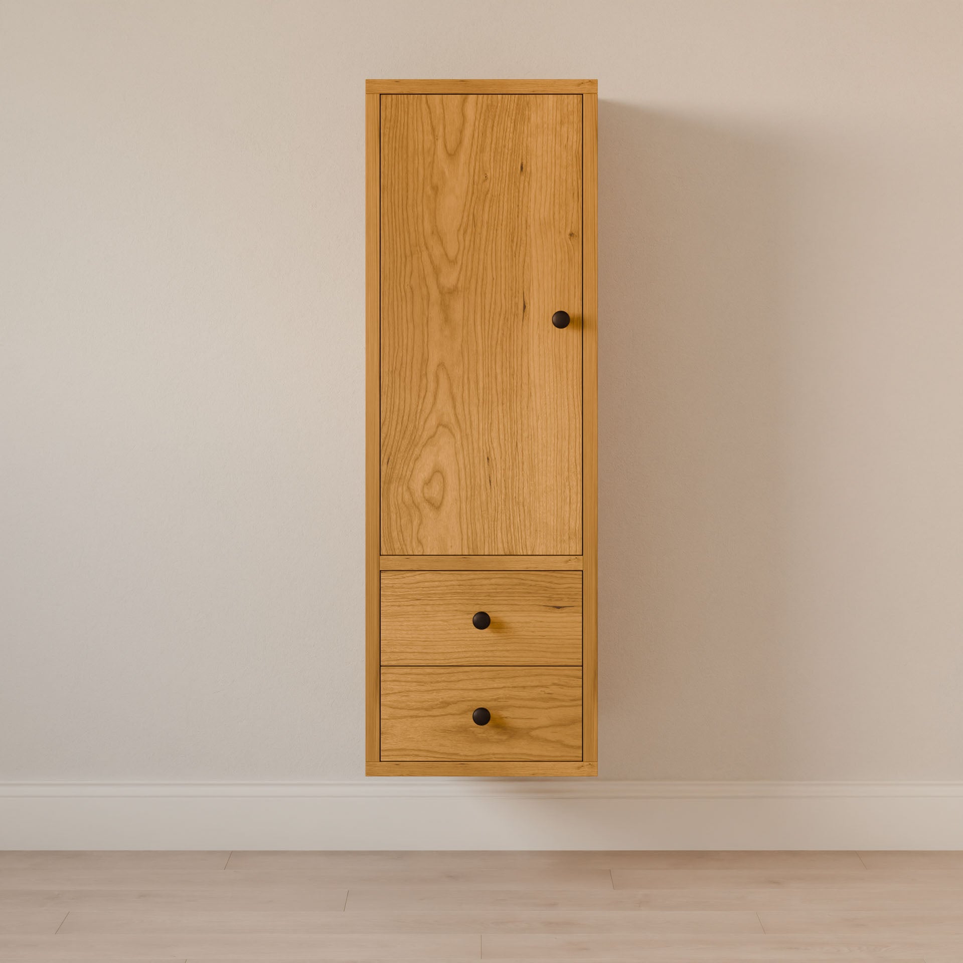 The Double Drawer Linen Cabinet in Cherry by Krovel Furniture Co. is crafted from solid hardwood with sustainable construction. It features a wall-mounted design, a small door at the top, and two drawers below, all accented by black knobs against a light-colored wall and floor.
