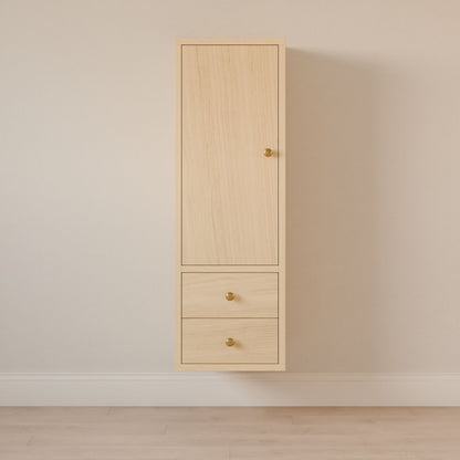The Maine Made Double Drawer Linen Cabinet by Krovel Furniture Co. features light wood hardwood, a tall upper door, and two lower drawers with gold knobs—perfect as a bathroom vanity cabinet against off-white walls and a light wood floor.