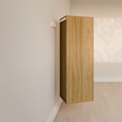The Maine Made Double Drawer Linen Cabinet by Krovel Furniture Co. is a tall, rectangular hardwood piece mounted on a light wall above a light wood floor, its shadow highlighted as sunlight and leaf patterns play across the background.