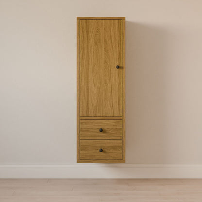 The Krovel Furniture Co. Maine Made Double Drawer Linen Cabinet, a solid hardwood wall-mounted unit with a top door and two lower drawers featuring black round knobs, is shown against a plain light-colored wall and light wood floor.