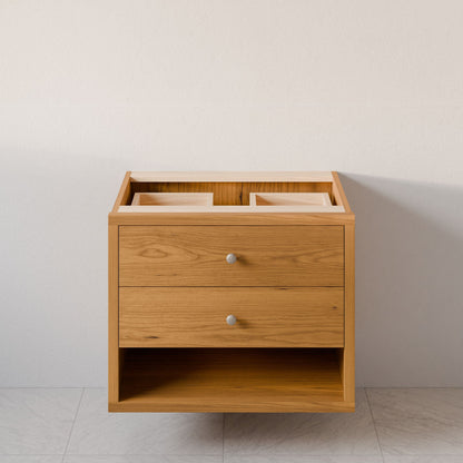 The Maine Made Double Drawer, Open Shelf Vanity by Krovel Furniture Co. is shown without a countertop or sink, featuring two drawers and an open shelf at the bottom against a light wall and tiled floor.
