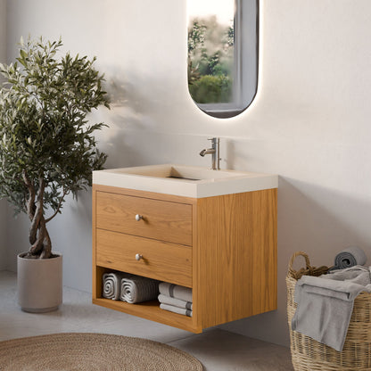 A modern bathroom featuring the Krovel Furniture Co. Maine Made Double Drawer, Open Shelf Vanity with a white sink, rolled towels on open shelves, a round-edged mirror above, an olive tree in a pot, and a wicker basket of towels on the floor.