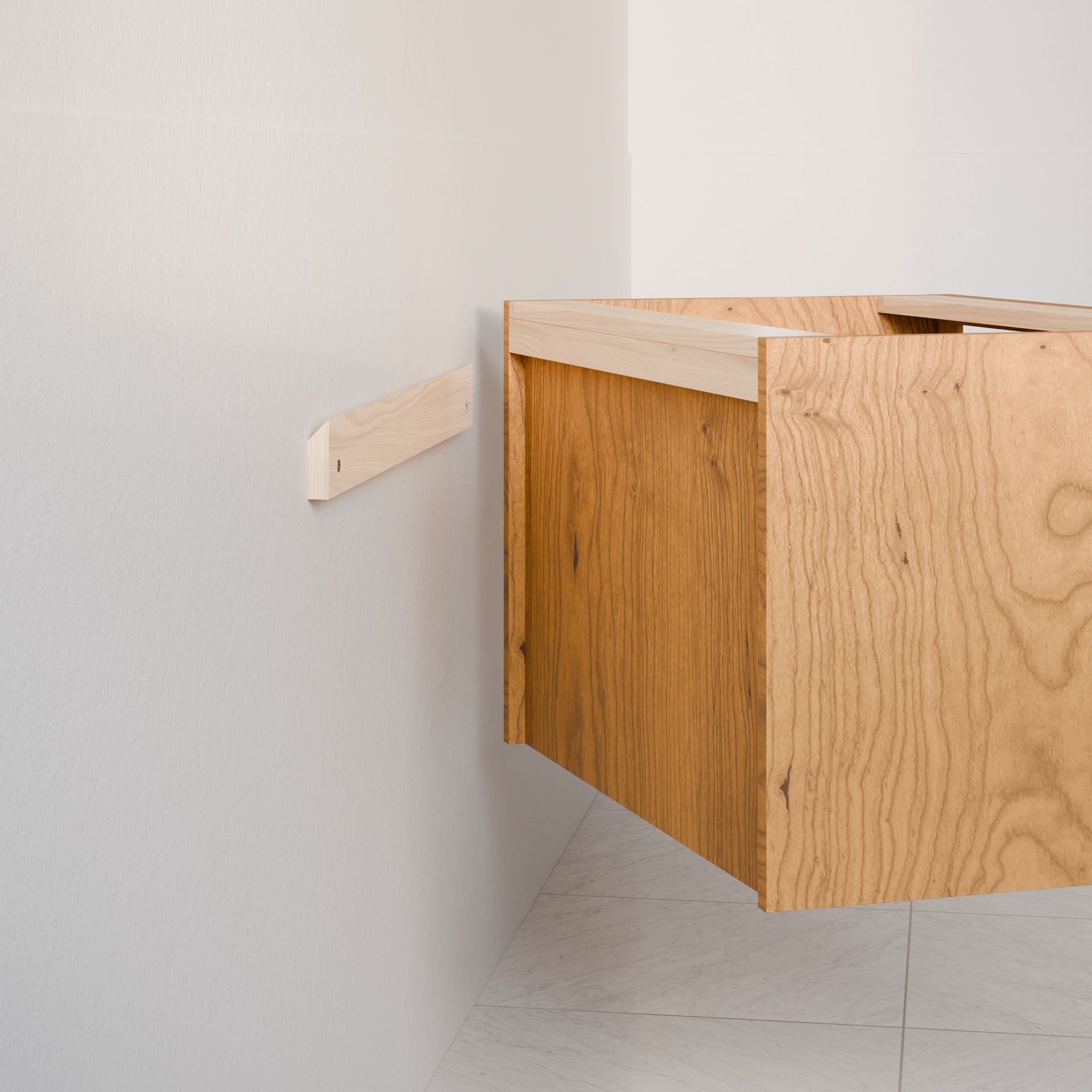 A custom-sized Double Drawer Vanity in Cherry by Krovel Furniture Co., with an open back revealing part of its interior support beam, is being mounted on a white wall. The hardwood veneer gives it a floating appearance, while the floor beneath has a light, speckled pattern.