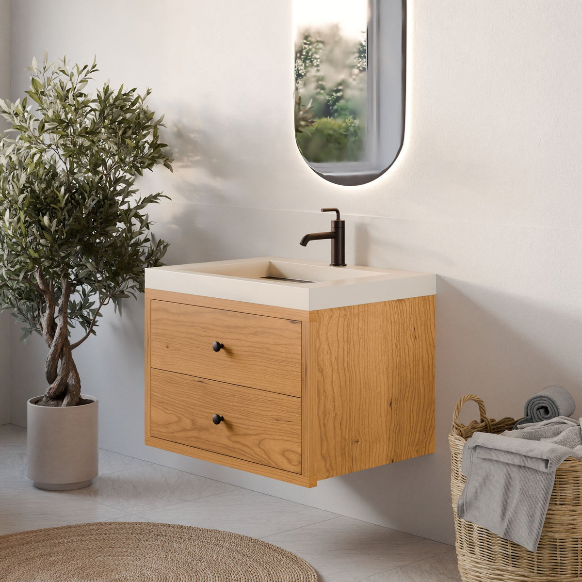 A bright, minimalistic bathroom features Krovel Furniture Co.'s Double Drawer Vanity in Cherry, topped with a rectangular white sink and black faucet. An oval mirror, potted plant, and woven basket of towels complete the tailored, modern look.
