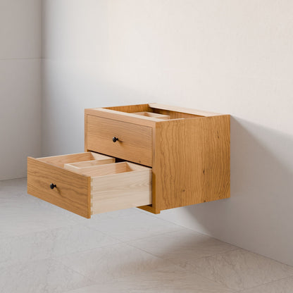 The Double Drawer Vanity in Cherry by Krovel Furniture Co. features two drawers, one partially open to reveal interior dividers, and is mounted on a white wall above a light tiled floor.