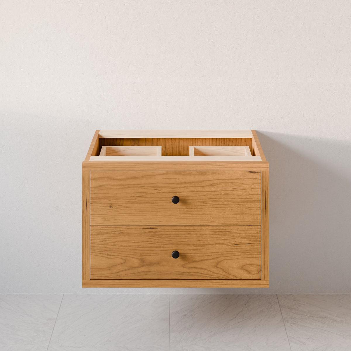 The Double Drawer Vanity in Cherry by Krovel Furniture Co. is a custom-size floating cabinet with hardwood veneer, two drawers with black knobs, and two open top compartments for sinks, mounted on a light wall above a tiled floor.