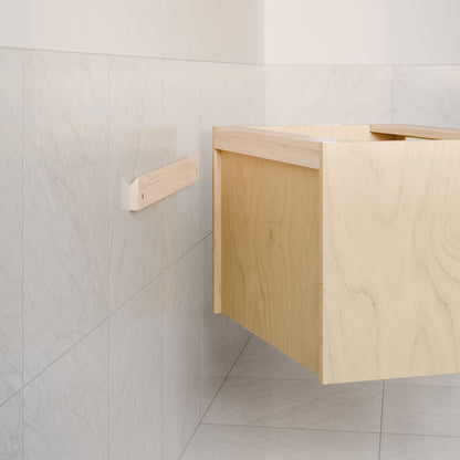 A corner of the room features light gray marble tile walls and floor. The partially visible Double Drawer Vanity in Maple from Krovel Furniture Co., with dovetail joinery, is elegantly suspended, exuding a minimalistic and modern charm.