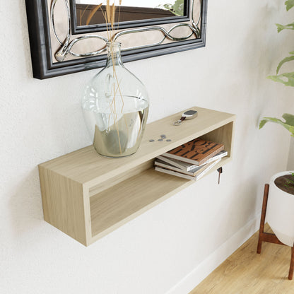 The Krovel Entryway Organizer in Maple, wall-mounted and stylish, is adorned with a large glass vase holding thin sticks, coins, and car keys on top. Inside sits a small pile of books. A nearby plant and framed mirror complete the chic setup.