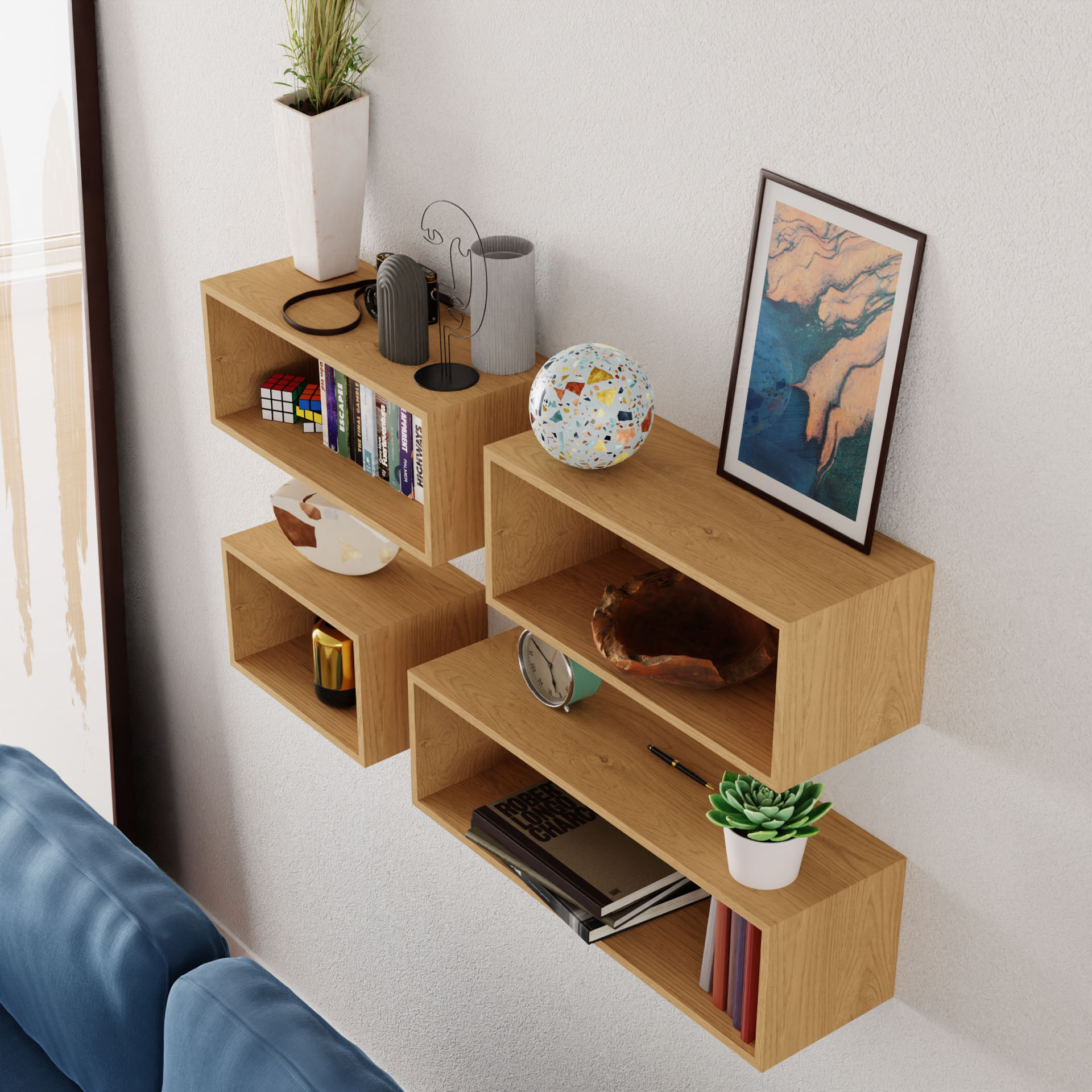 The "Floating Bookshelf in Maple" by Krovel, crafted from solid American hard maple, elegantly displays books, a framed painting, potted plants, a decorative globe, and small decor items. Mounted above a blue sofa, they lend a cozy and artistic ambiance with their handmade charm.