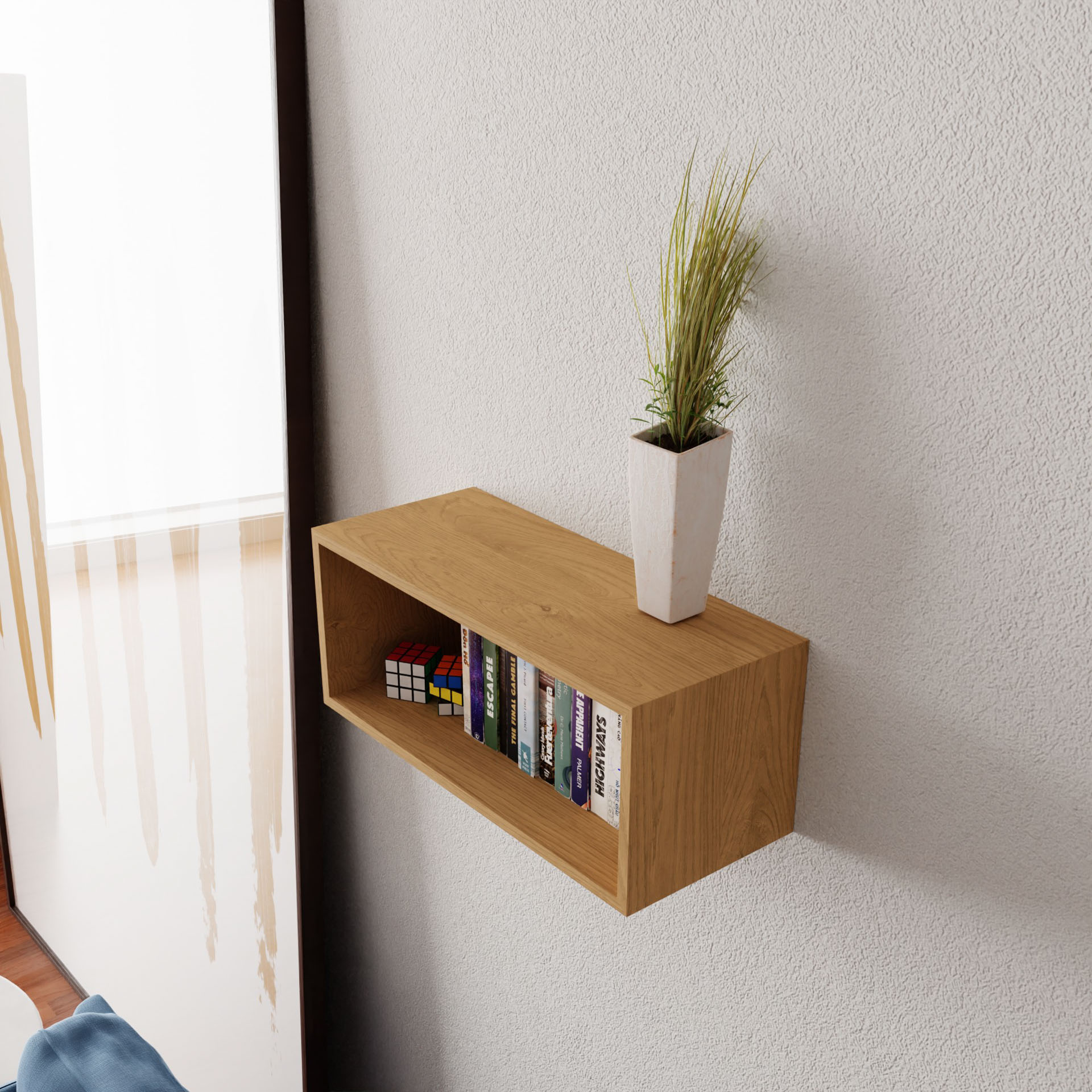 The Krovel Floating Bookshelf in Maple, made from solid American hard maple, supports a few books and a white vase with grass-like plants. Abstract brown and beige art decorates the nearby wall while the handmade shelf's shadow adds depth to the textured surface.