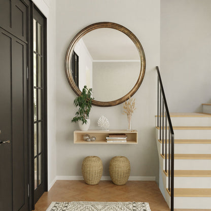 A modern entryway showcases a large round mirror above a Krovel Hardwood Floating Console Table displaying decor, a plant, and books. Two woven baskets are placed beneath the shelf, with a staircase visible on the right.
