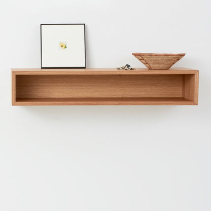 The Krovel Hardwood Floating Console Table is mounted on a white wall, displaying a square framed picture, small woven basket, and set of keys. Its simple, minimal design adds mid-century modern charm to any space.