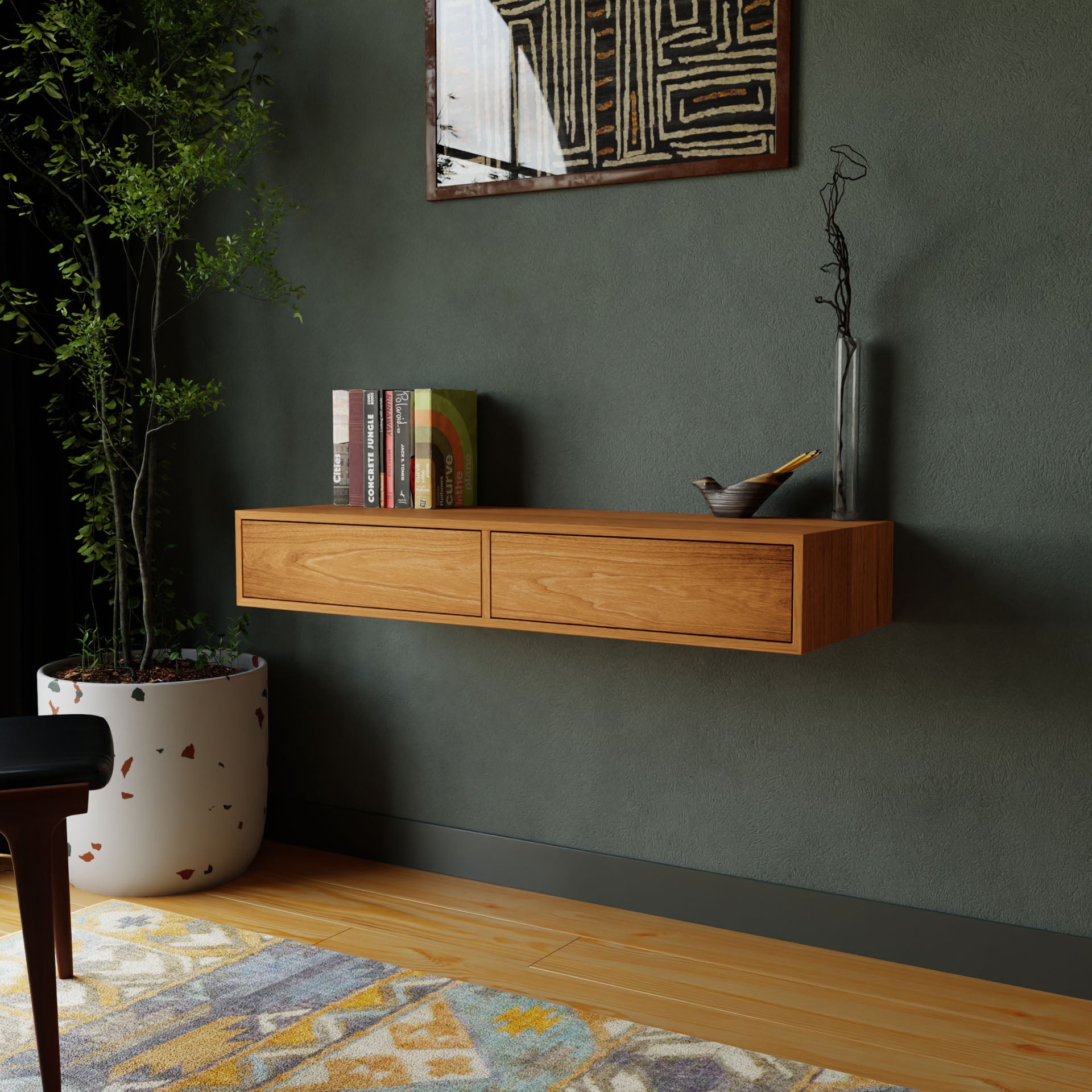 A modern living room features Krovel's Floating Desk in Cherry, adorned with books and a vase. A decorative bowl adds charm to the display against a dark green wall with abstract art. A large potted plant and part of a rug enhance the wooden floor.