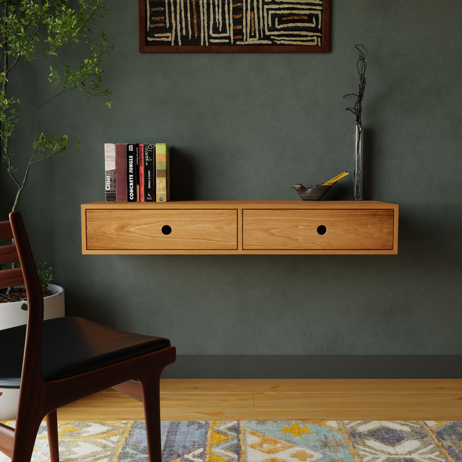 A minimalist room features a Krovel Floating Desk in Cherry, displaying books and a small sculpture. Beneath, a patterned rug adorns the wooden floor. A chair is partially visible on the left, with a plant standing in the corner against a textured green wall.