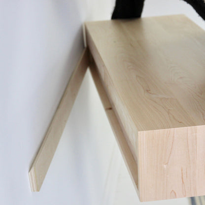 A Krovel Floating Desk in Maple is being installed on a white wall. One bracket is attached, and another is partially slid into the mounted piece, aligning the desk for placement. The natural maple wood grain enhances its elegance.