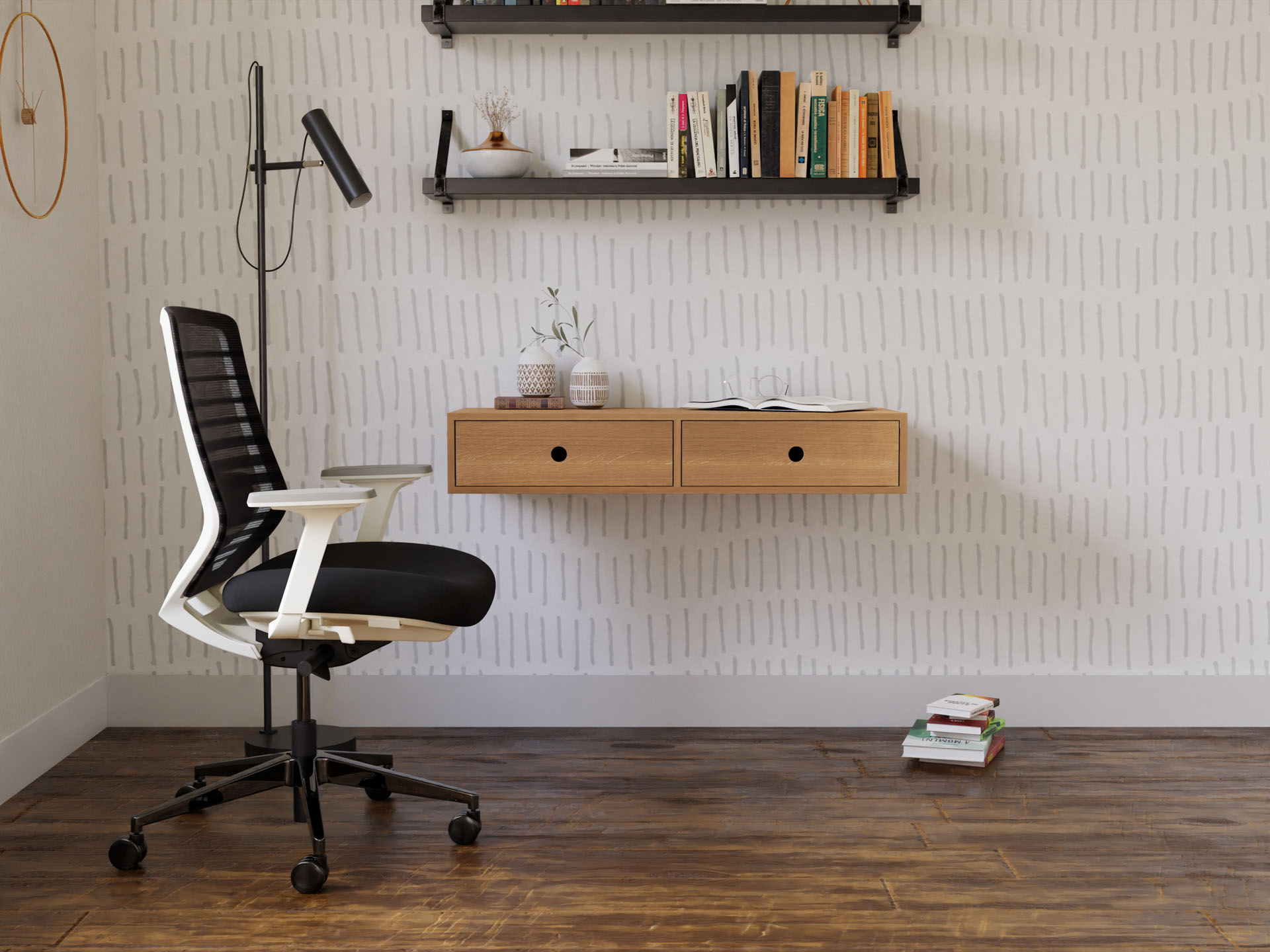 A modern office features a hand-finished black and white ergonomic chair on a wooden floor. A wall-mounted Krovel floating desk in White Oak holds a vase and books. Above, two shelves showcase books and decor against patterned wallpaper, while a tall black lamp stands nearby.