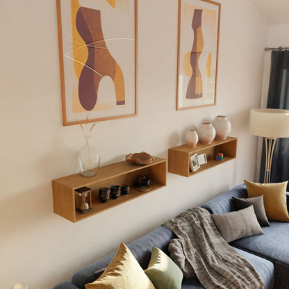 A cozy living room with a blue sofa, assorted pillows, plaid throw, and Krovel Hardwood Floating Display Case showing vases and decor. Two abstract art prints hang above the sofa, with a floor lamp in the corner.