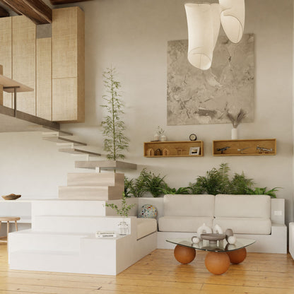 Modern living room with minimalist decor, a white sofa, glass coffee table with round brown legs, potted plants, Krovel Hardwood Floating Display Case, abstract wall art, and a light wood staircase leading to a loft.