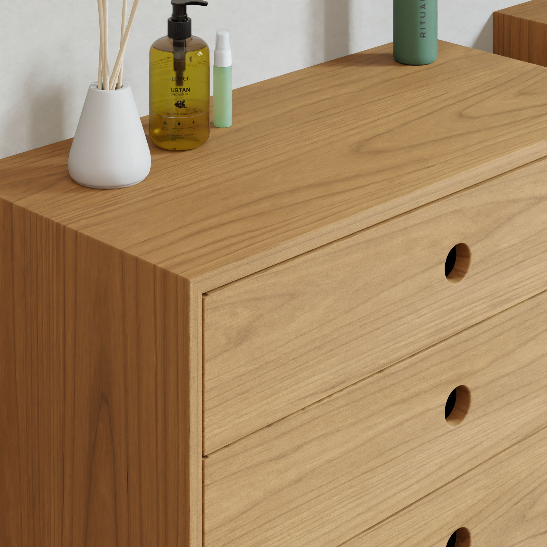 The Krovel Floating Dresser in Cherry is oversized and crafted from hand-finished hardwood, featuring three drawers with circular cut-out handles. Adorning the top are a white vase with reeds, a yellow bottle, a small spray, and a green cylindrical container against a light-colored wall backdrop.