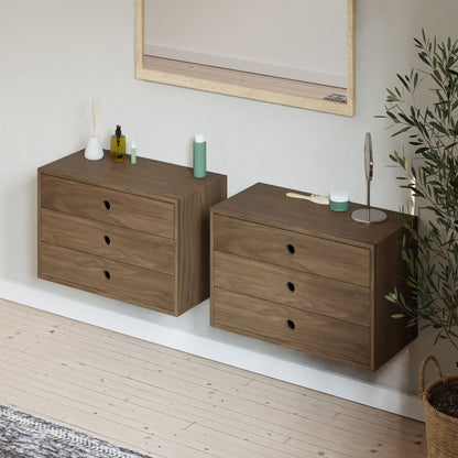 Two Krovel Floating Dressers in Walnut, each with three drawers and soft-close premium slides, sit below a large rectangular wall mirror. Items like a small plant, bottles, and a hairbrush are on the dressers. A potted plant is nearby on the floor.