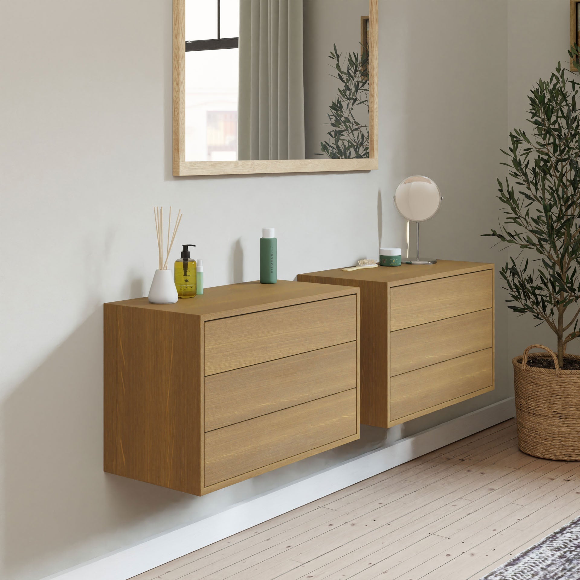 Two Krovel Hardwood Floating Dressers, each with three drawers, are mounted on a light-colored wall beneath a large mirror. Decorative items sit atop the dressers, and a potted plant rests on the wooden floor nearby.