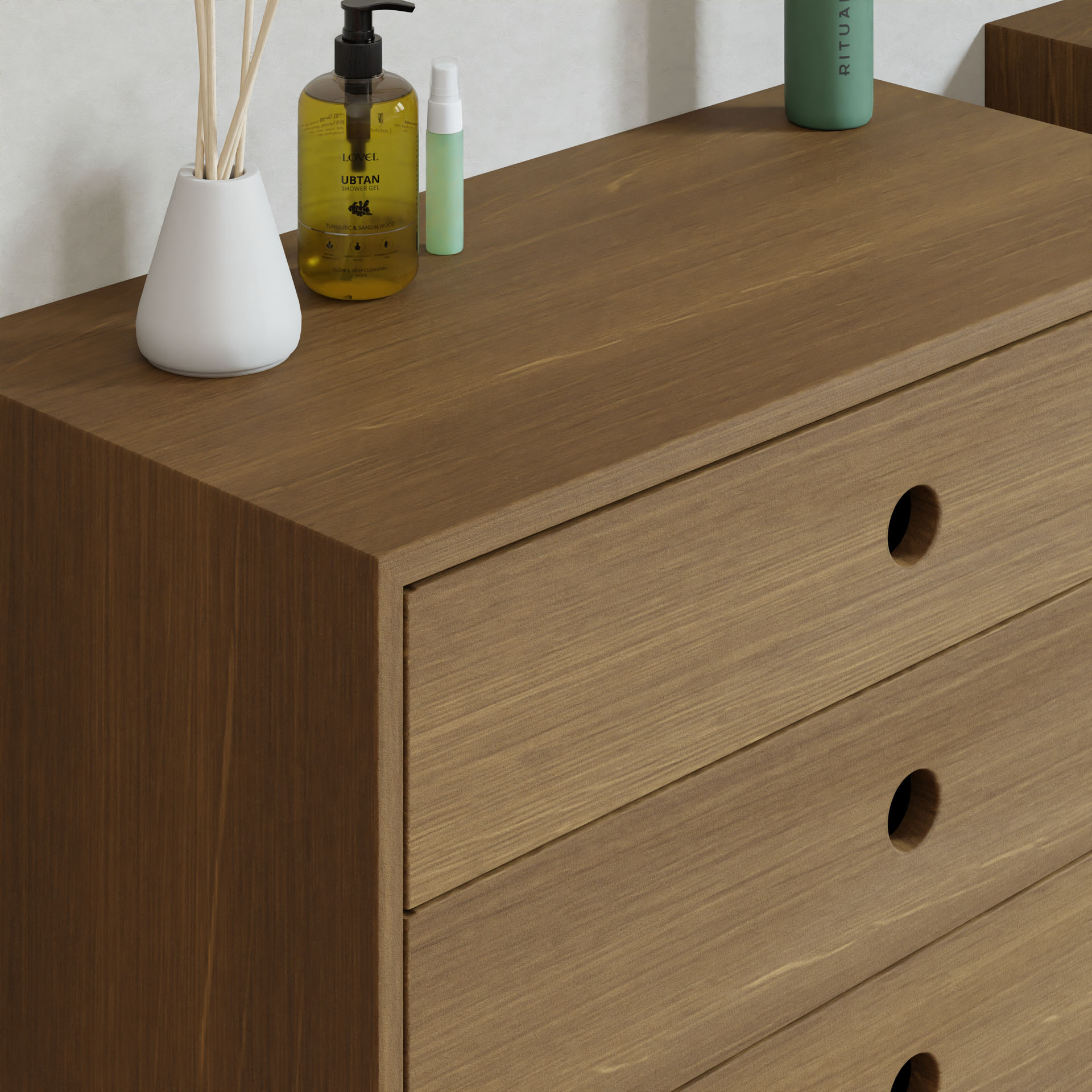A Krovel Floating Dresser in white oak with three drawers and simple round handles holds a reed diffuser, yellow bottle with pump, and green cylindrical container, all set against a plain white wall.