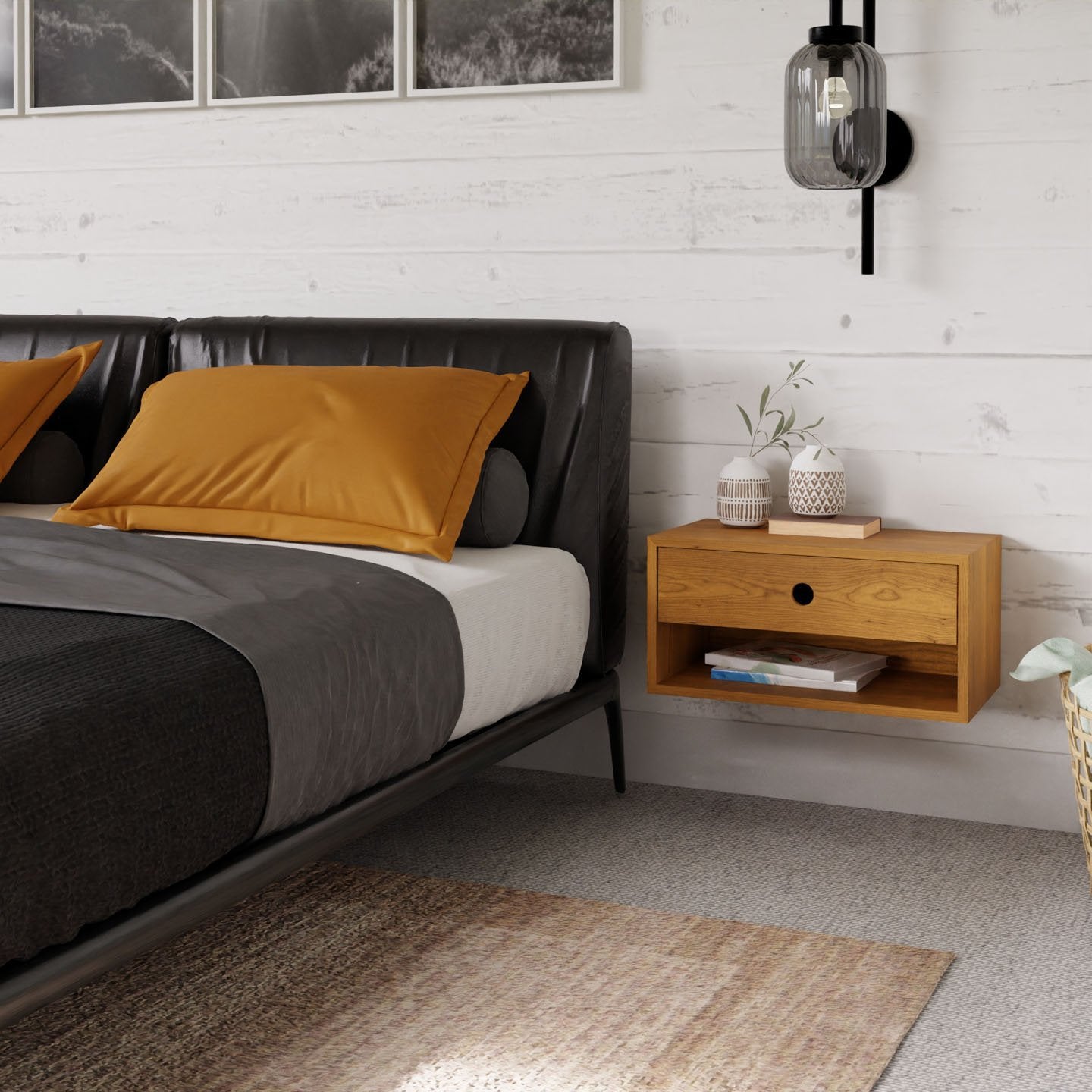 A modern bedroom features a dark upholstered bed, mustard yellow pillows, gray bedding, and the Krovel Hardwood Double Floating Nightstand with decor, plus white paneled walls, a black wall sconce, and framed photos above the bed.