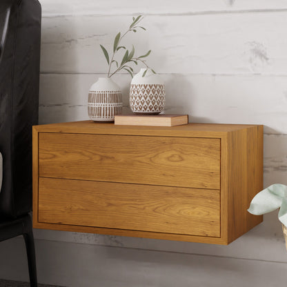 The Krovel Hardwood Double Floating Nightstand, featuring two drawers, is mounted on a white shiplap wall with decorative vases, a small plant, and a book on top; a black chair and green plant are nearby.