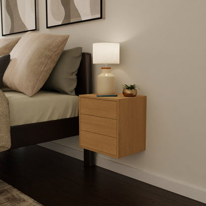 A modern bedroom showcases the Krovel Hardwood Triple Floating Nightstand with a white lamp, potted plant, and book beside a bed with beige bedding, all beneath abstract art.