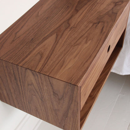 A detailed look at the Krovel Hardwood Double Floating Nightstand, crafted from solid hardwood with a smooth finish, visible natural grain, a drawer, and open compartment—sleekly mounted on a white wall.