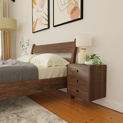 A modern bedroom with a solid hardwood bed, cream bedding, and the Krovel Hardwood Triple Floating Nightstand topped with a lamp, plant, and vase. Two abstract art pieces hang above the bed as sunlight brightens the cozy space.