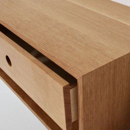Close-up of the Krovel Floating Nightstand in White Oak, crafted from solid American White Oak, with a slightly open drawer revealing its inner compartment. The surface features a smooth, natural finish that highlights the wood grain. This soft-close drawer includes a circular cutout handle for easy access, making it an ideal addition to any room. 