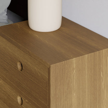 Close-up of a solid Floating Nightstand in White Oak by Krovel, showcasing two soft-close drawers with circular cutout handles. A white cylindrical vase is placed on top, with part of a light gray cushion or bedding visible in the upper left corner. 