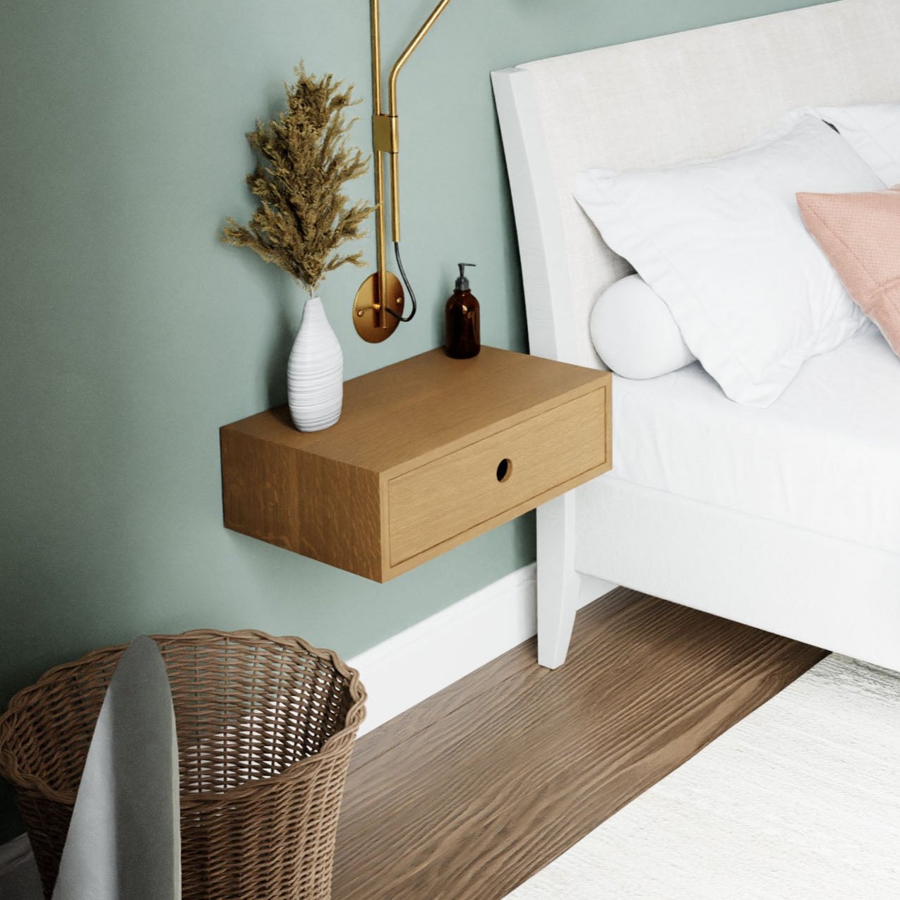 In a snug bedroom corner, a white bed adorned with pillows is paired with Krovel's Floating Nightstand in White Oak. The nightstand displays a vase of dried flowers and a soap dispenser. On the floor, there's a basket, and a wall-mounted lamp casts warm light on the pale green wall. #configuration_single-drawer