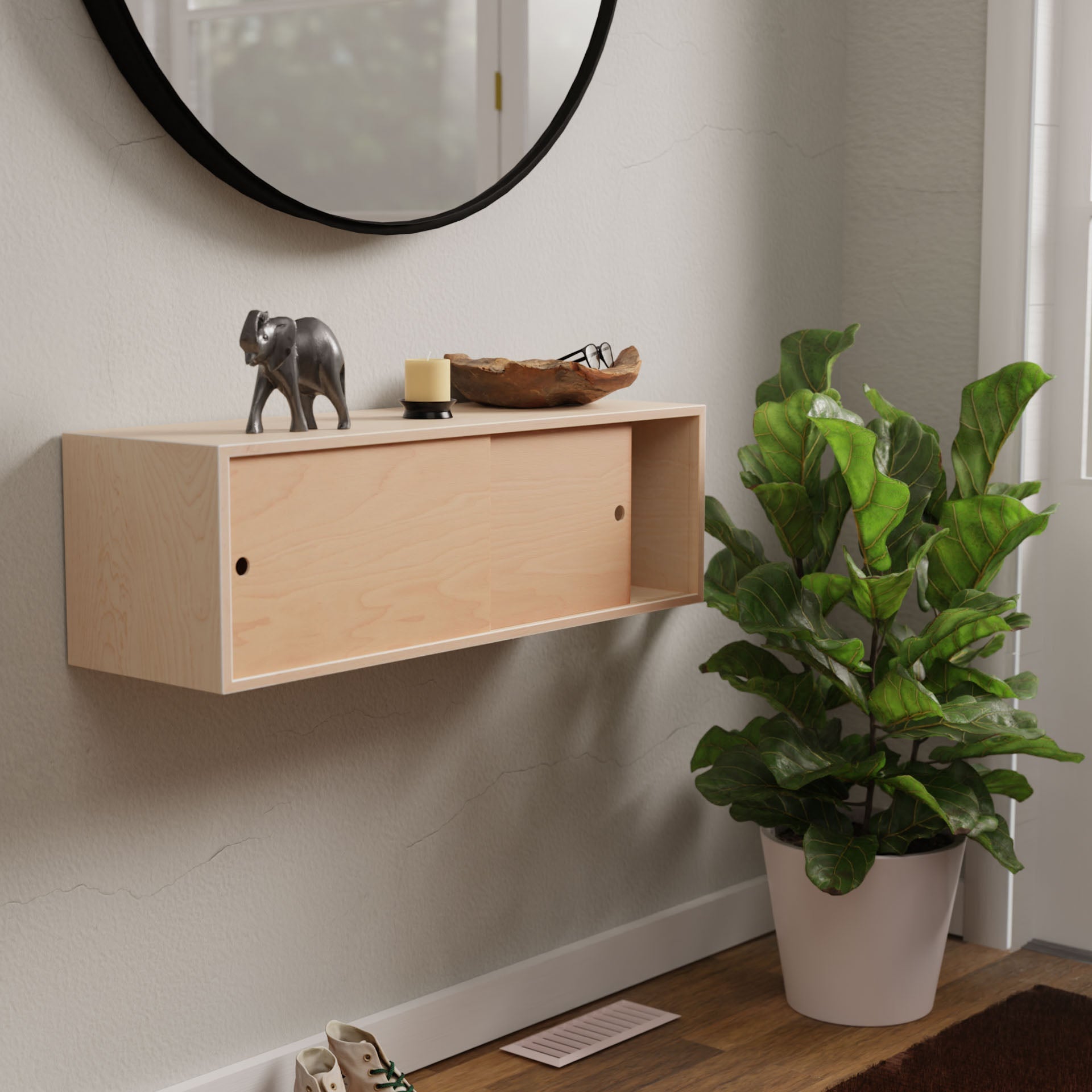 A minimalistic entryway features the Krovel Floating Storage Cabinet in Maple adorned with a decorative elephant figurine, candle, and glasses. Elegantly paired with a potted floor plant near a round wall mirror, partially visible shoes complete the scene.