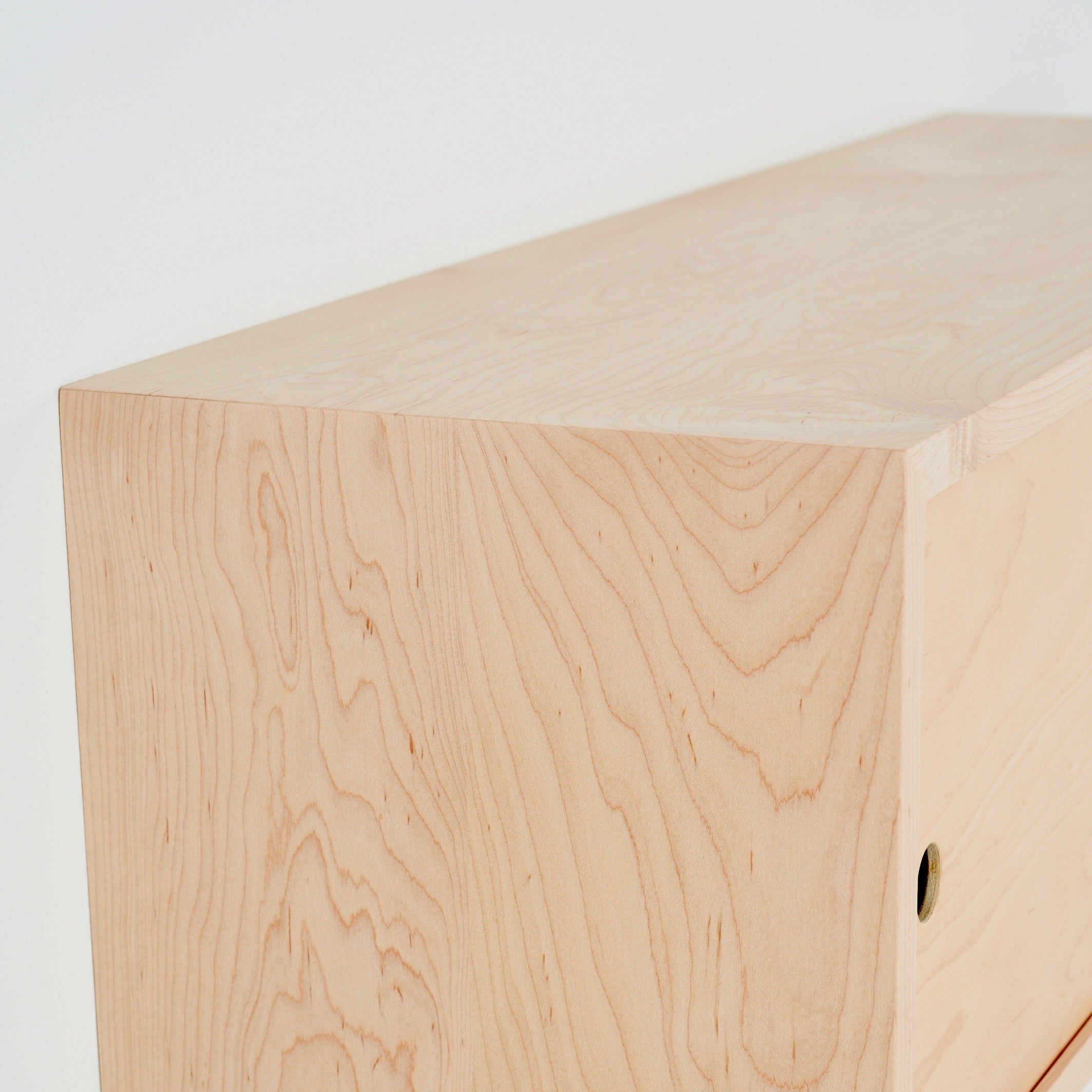 A close-up of the corner of Krovel's Floating Storage Cabinet in Maple showcases the wood grain patterns. The smooth, light finish features a small circular hole near the edge, set against a plain white background.