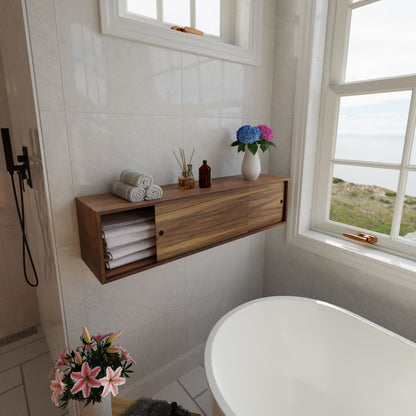 A bright bathroom features a Krovel Hardwood Floating Storage Cabinet for towels and decor, a white bathtub, fresh flowers, and large windows with scenic views of water and greenery.